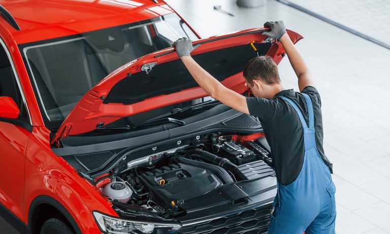 Top view of male worker in uniform that repairs red automobile