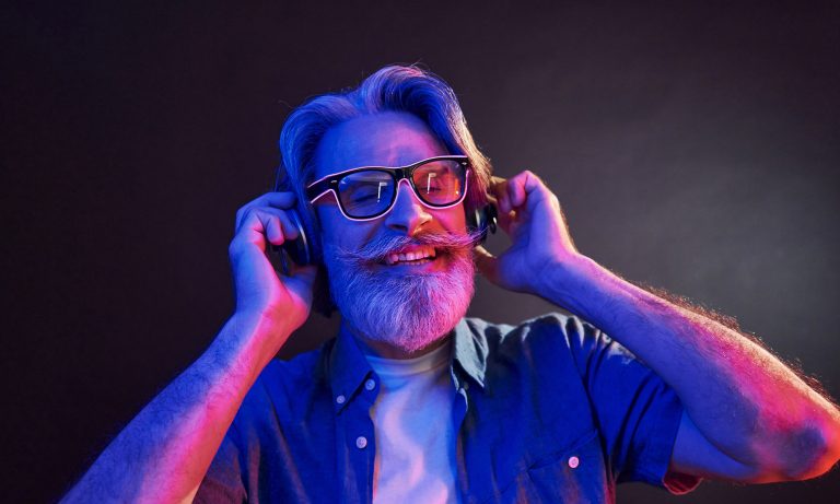 Neon lighting. In headphones. Stylish modern senior man with gray hair and beard is indoors